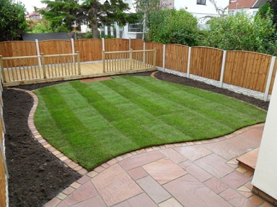 A newly turfed lawn with a curved brick edge, sandstone patio and timber deck.